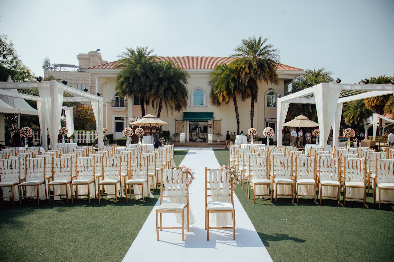 Beautiful outdoor wedding ceremony setup with rows of decorated chairs facing a luxurious villa.